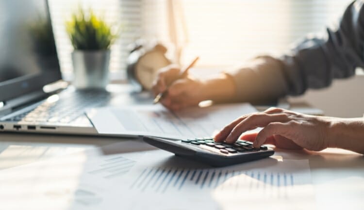 man uses a calculator while writing in tax forms