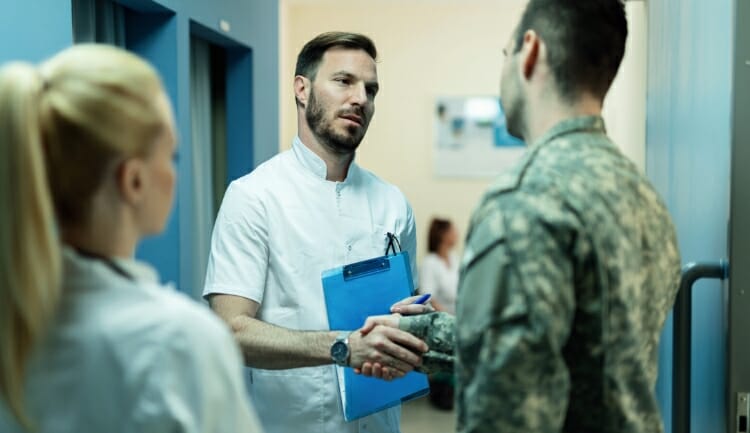 a doctor and a man in army digital camo shake hands in a hospital